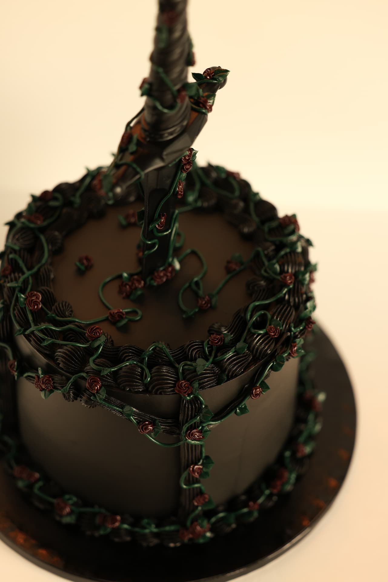 Black cake wrapped in piped vines and burgundy roses with a dark sword through the top