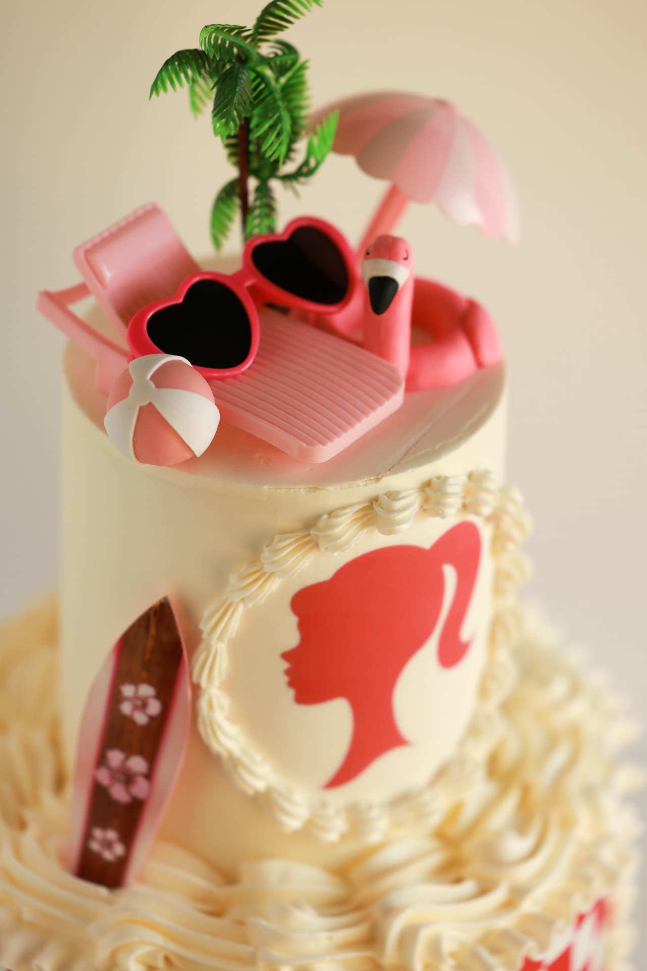 Beach party cake topped with pink sunglasses, a flamingo float, palm tree and surfboard