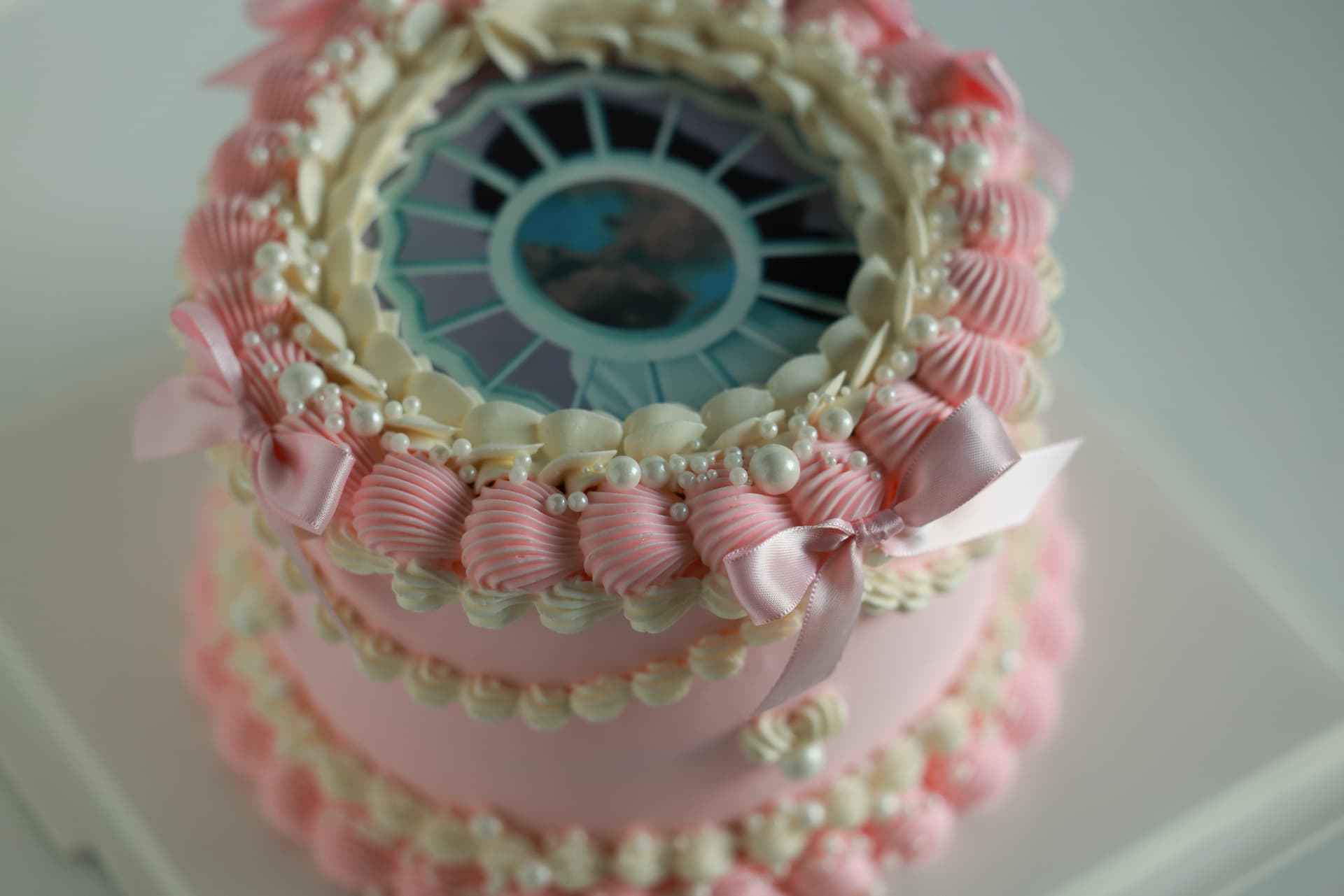 Two-tier pink vintage cake with piped shells, pearls, satin bows and a photo centerpiece