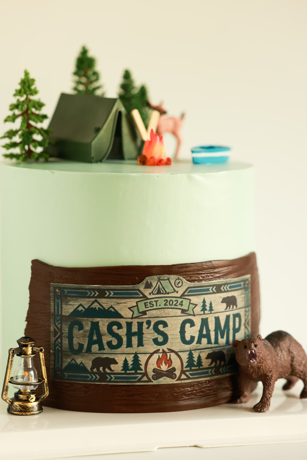 Mint camping cake with a chocolate wrap, a custom Cash's Camp sign, tent, campfire and bear toppers