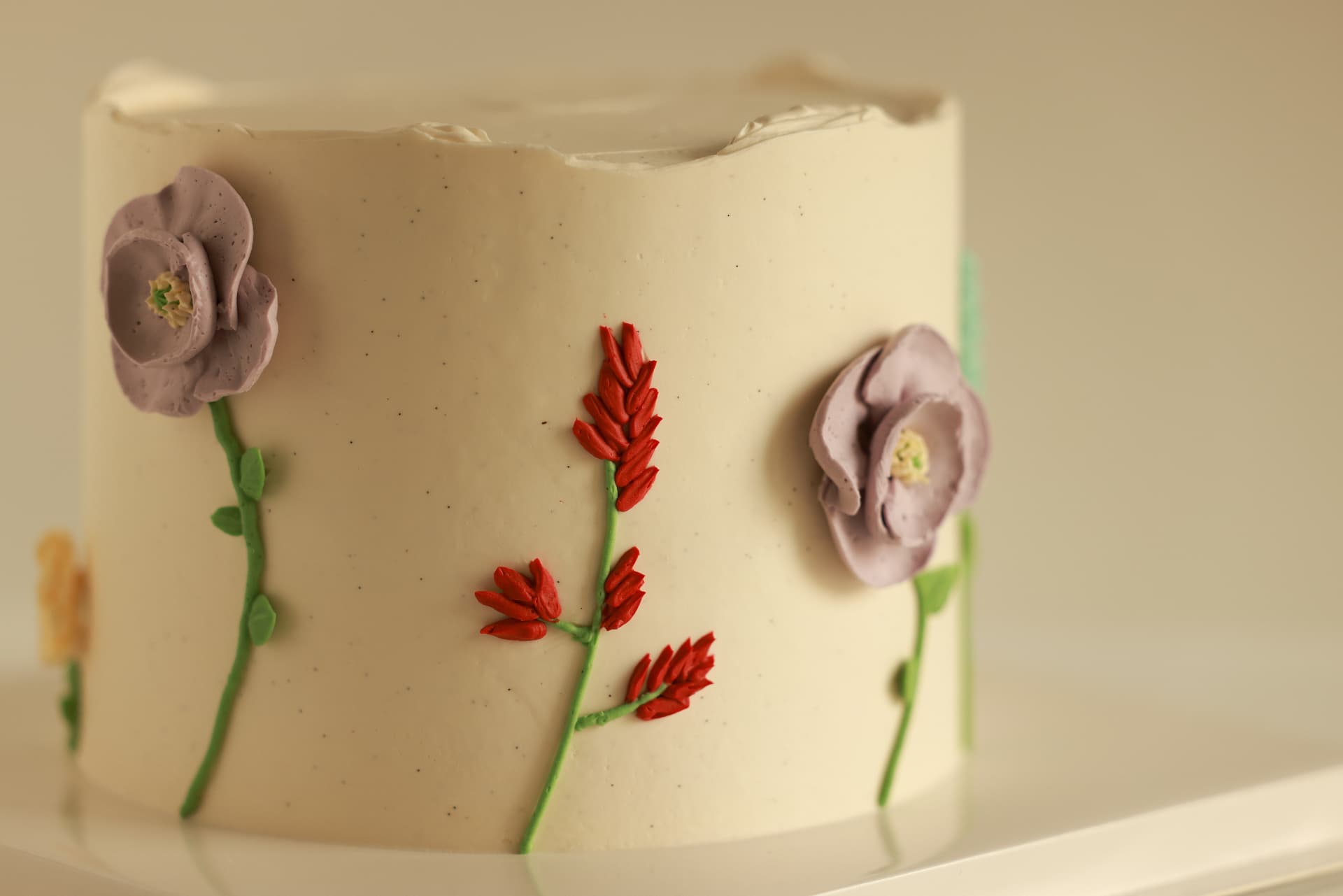 Vanilla buttercream cake decorated with hand-piped lavender roses, red wildflowers and green stems