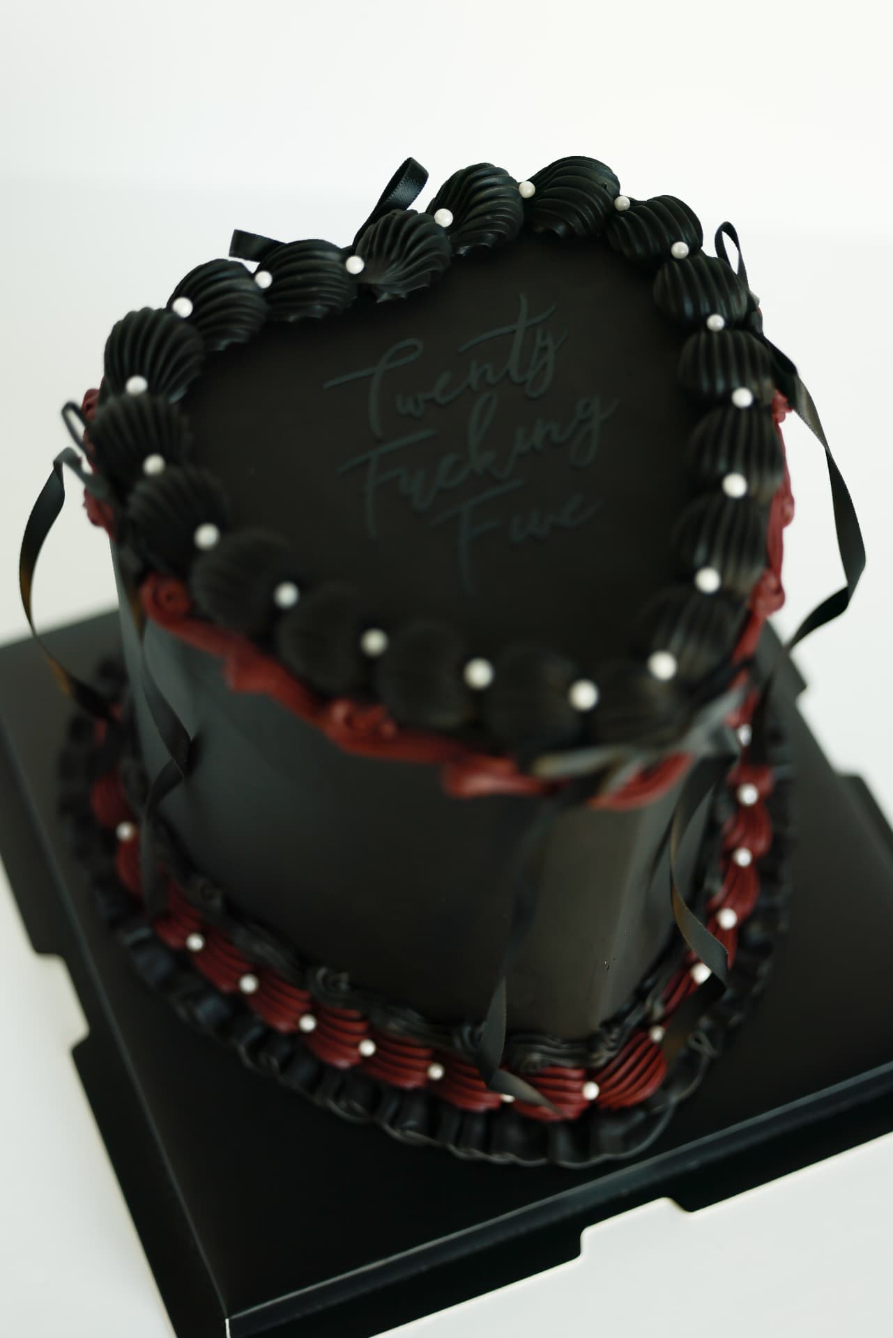 Black heart-shaped cake with burgundy piping, pearls and black satin ribbons
