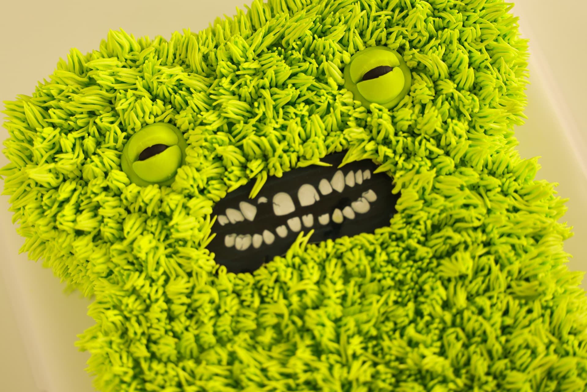 Fuzzy green monster cake with googly eyes and a big grin full of piped teeth