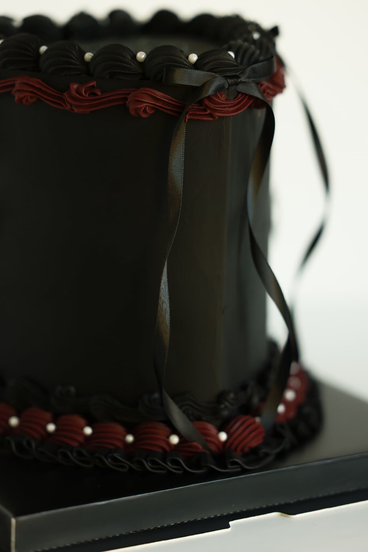 Elegant black cake with burgundy and black piped details, pearls and satin ribbon