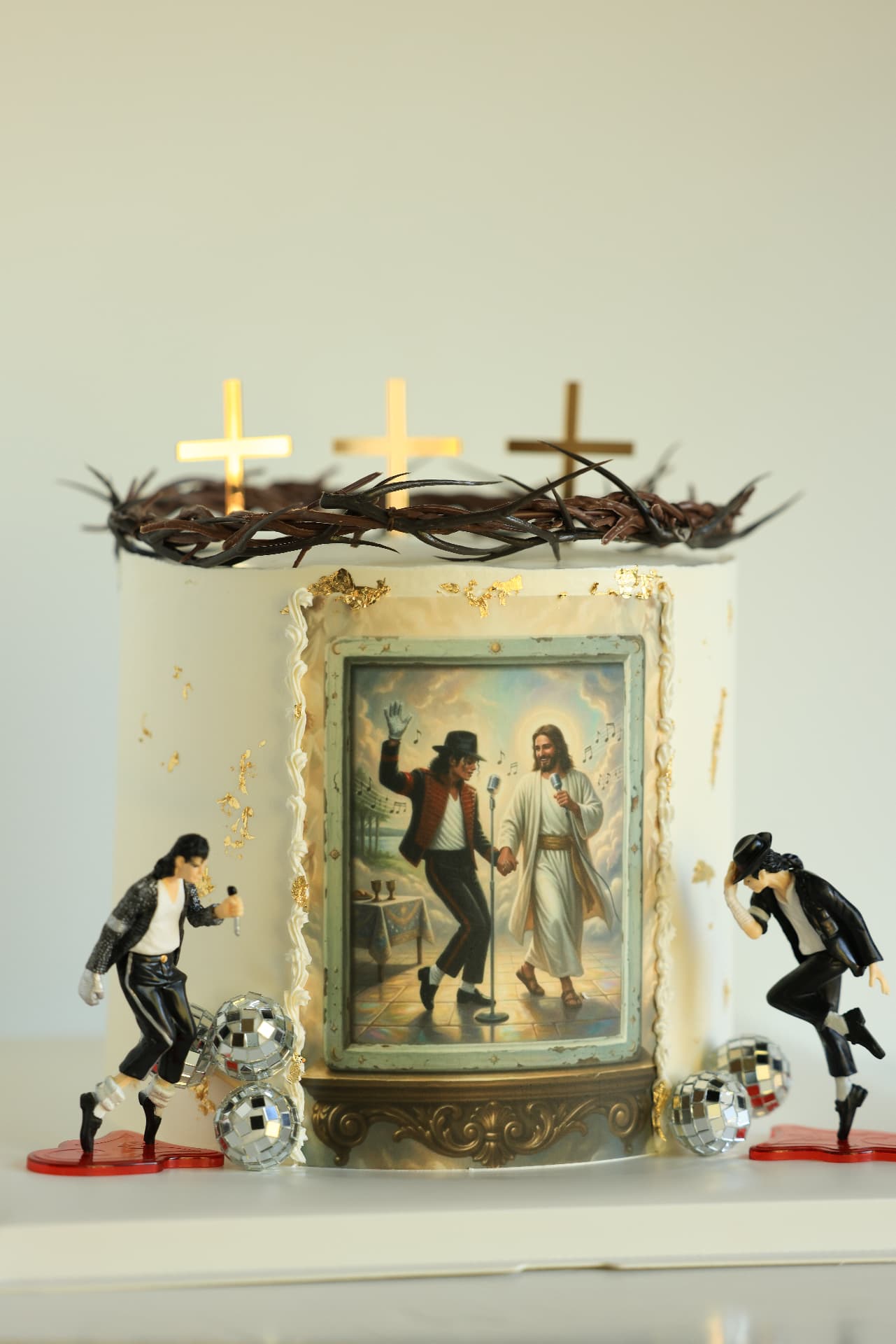 Cream cake with gold crosses, a crown of thorns, a framed dancing picture and Michael Jackson figurines with disco balls